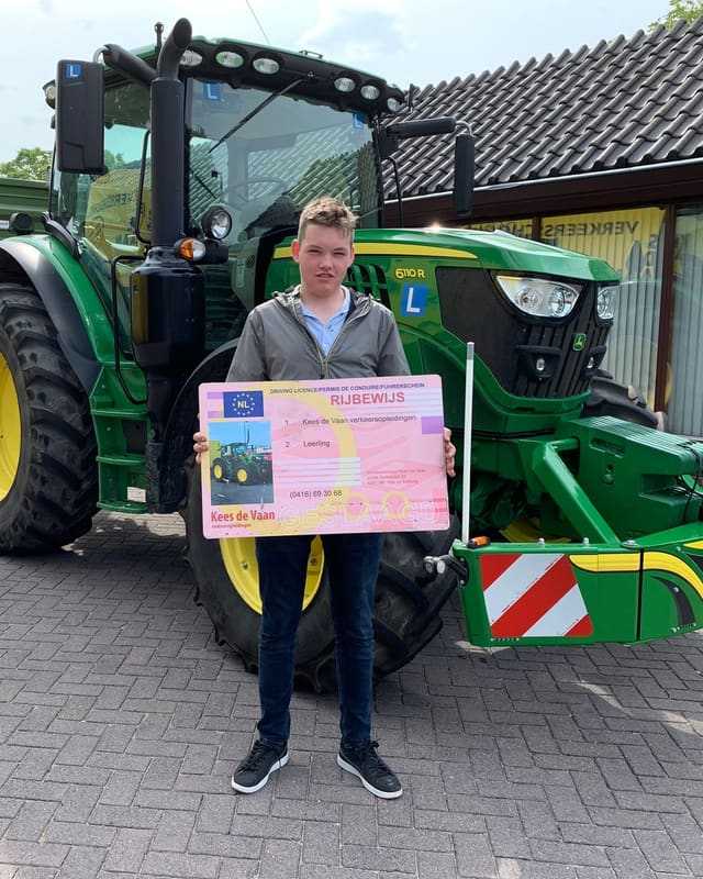 Geslaagde cursist in grijze trui met rijbewijsbord voor een groene lestrekker