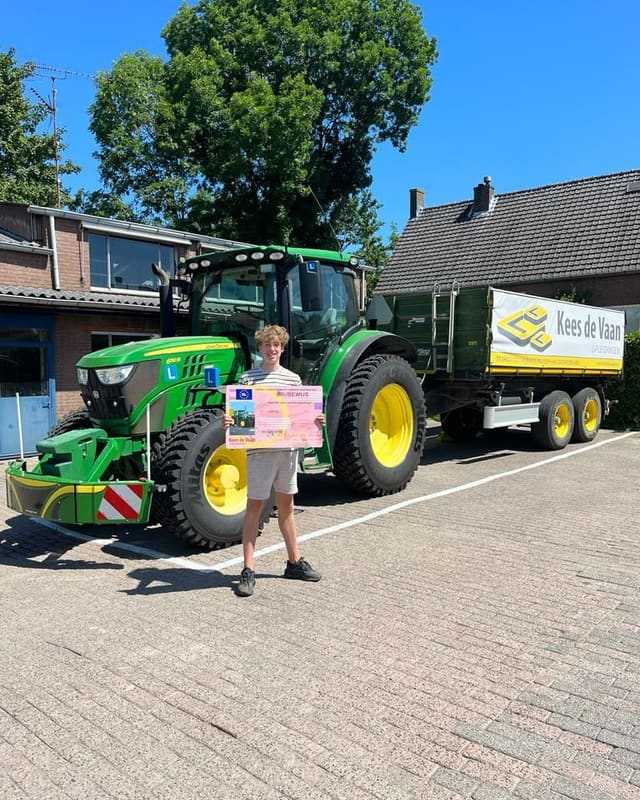 Geslaagd voor het T-rijbewijs: cursist in wit shirt en korte broek met rijbewijsbord bij de lestrekker met kipper