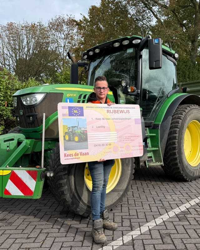 Geslaagd voor het trekkerrijbewijs: cursist met rijbewijsbord voor een groene lestrekker in de herfst