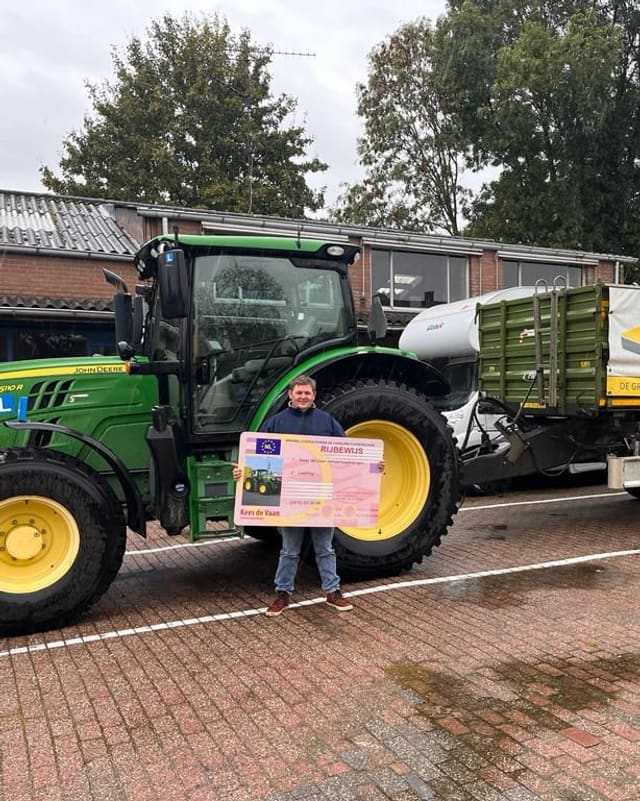 Geslaagd voor het trekkerrijbewijs: cursist in donkerblauwe trui met rijbewijsbord bij een groene lestrekker