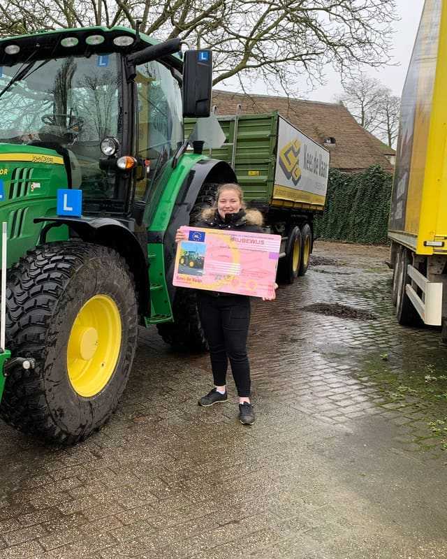 Geslaagde cursist met rijbewijsbord naast een groene lestrekker op een natte dag