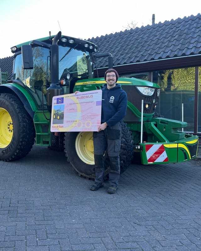 Geslaagd voor het T-rijbewijs: cursist met muts en rijbewijsbord naast een groene lestrekker