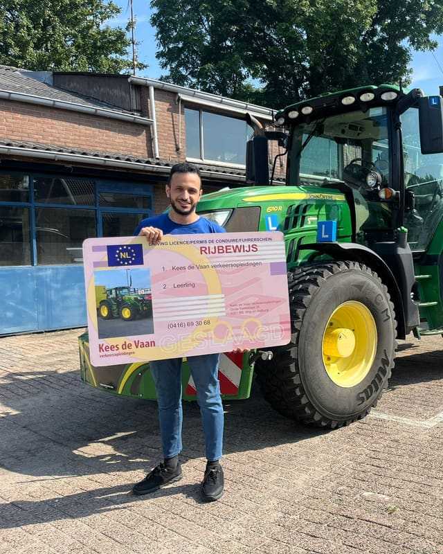 Geslaagd voor het T-rijbewijs: cursist in blauw shirt met rijbewijsbord bij de lestrekker