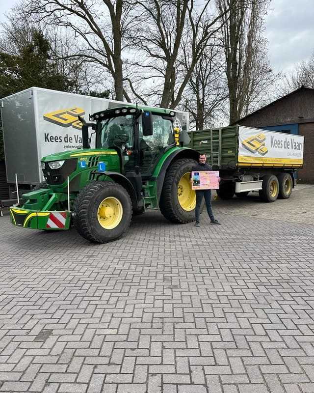 Geslaagde cursist met rijbewijsbord naast een groene lestrekker met aanhangwagen