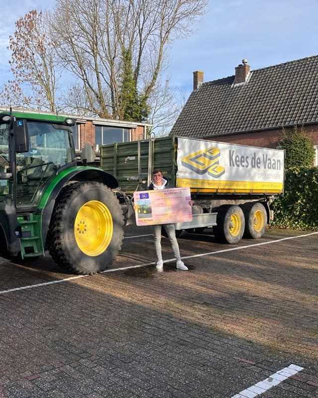 Geslaagde cursist met rijbewijsbord naast een groene lestrekker met kipper