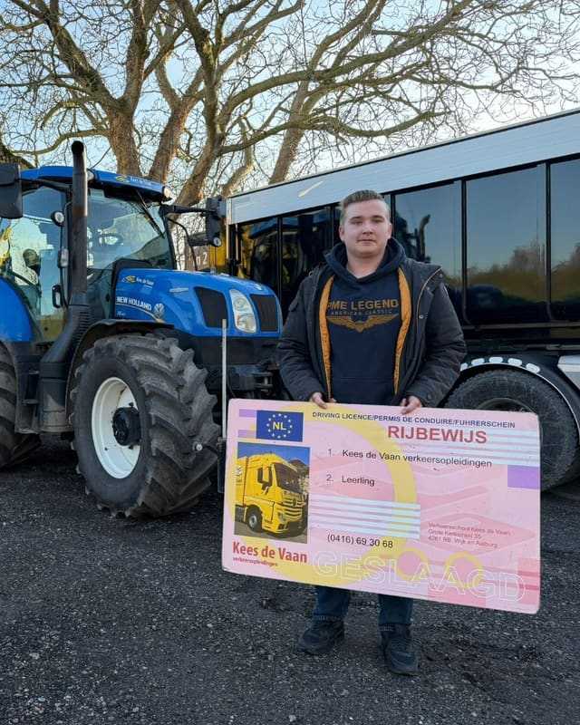 Geslaagd voor het trekkerrijbewijs: cursist met rijbewijsbord naast een blauwe lestrekker
