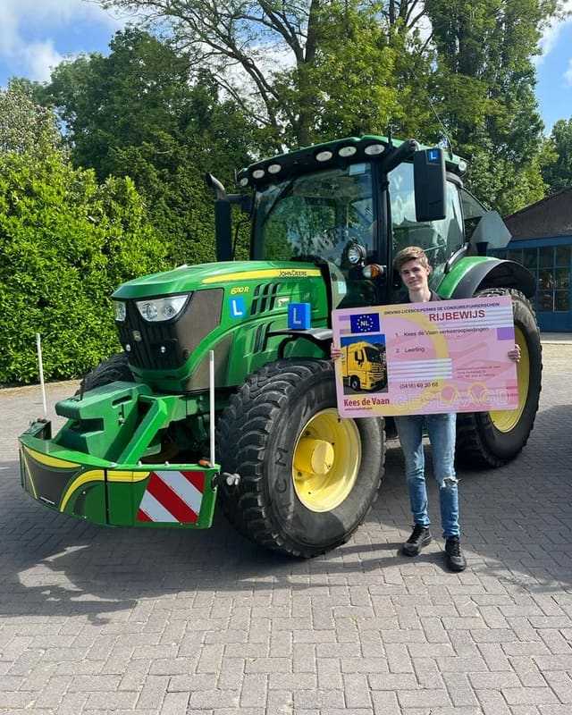Geslaagde cursist met rijbewijsbord voor een groene lestrekker met L-bord op de motorkap