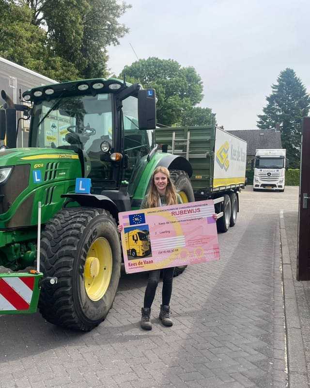 Geslaagd voor het T-rijbewijs: cursist met rijbewijsbord naast de lestrekker en een lesvrachtwagen