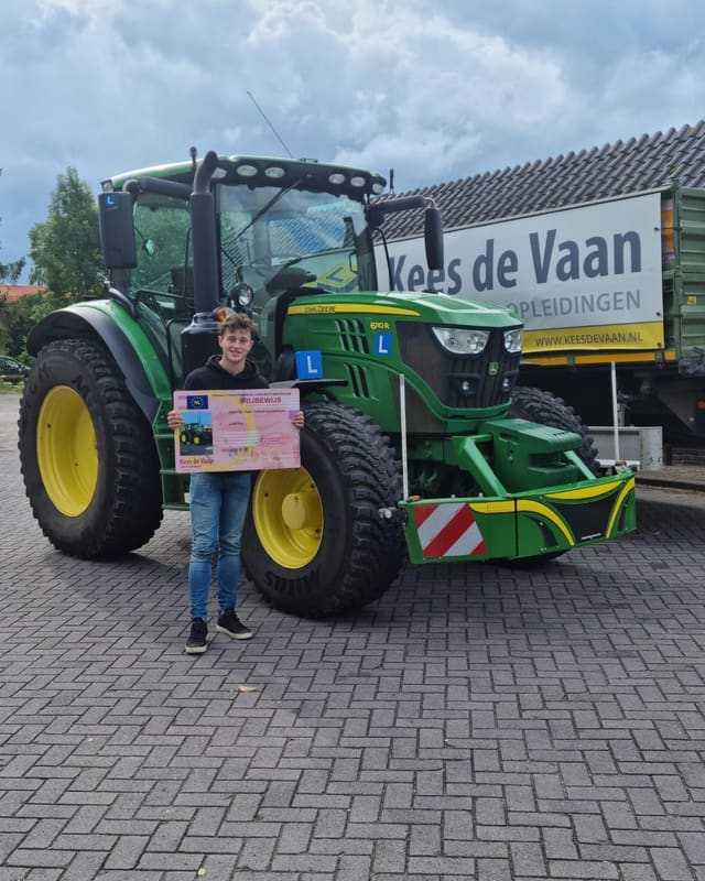 Geslaagde cursist met rijbewijsbord voor een groene lestrekker en het spandoek van Kees de Vaan