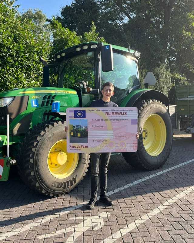 Geslaagd voor het trekkerrijbewijs: cursist met rijbewijsbord voor een groene lestrekker bij de heg