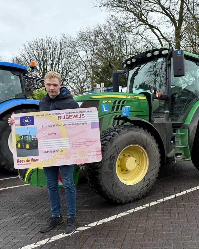 Geslaagde cursist met groot rijbewijsbord naast een groene lestrekker