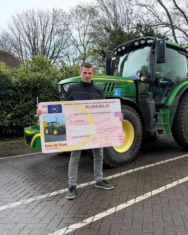 Geslaagde cursist met rijbewijsbord voor een groene lestrekker en kale bomen
