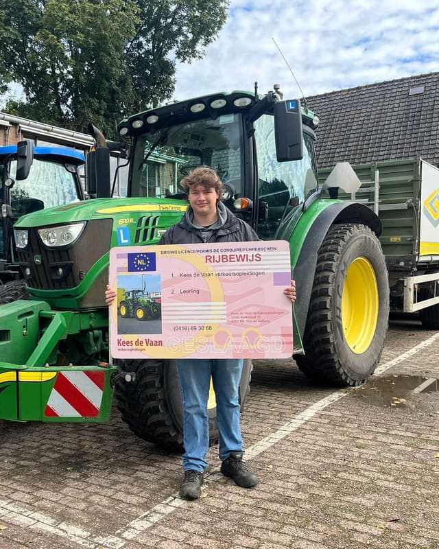 Geslaagd voor het trekkerrijbewijs: cursist met rijbewijsbord voor een groene lestrekker op het lesterrein