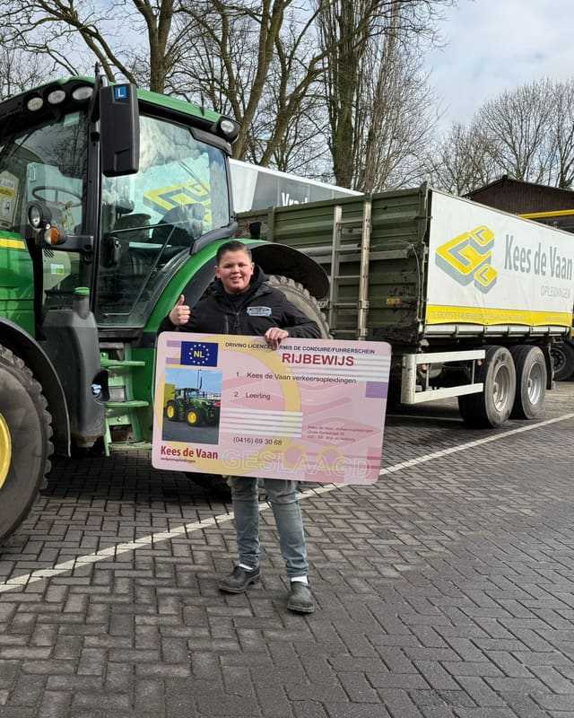 Geslaagd voor het T-rijbewijs: cursist met rijbewijsbord voor een groene lestrekker met kipper van Kees de Vaan