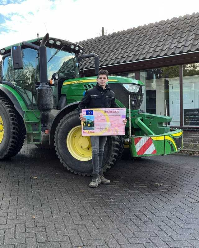 Geslaagde cursist met rijbewijsbord voor de bumper van een groene lestrekker