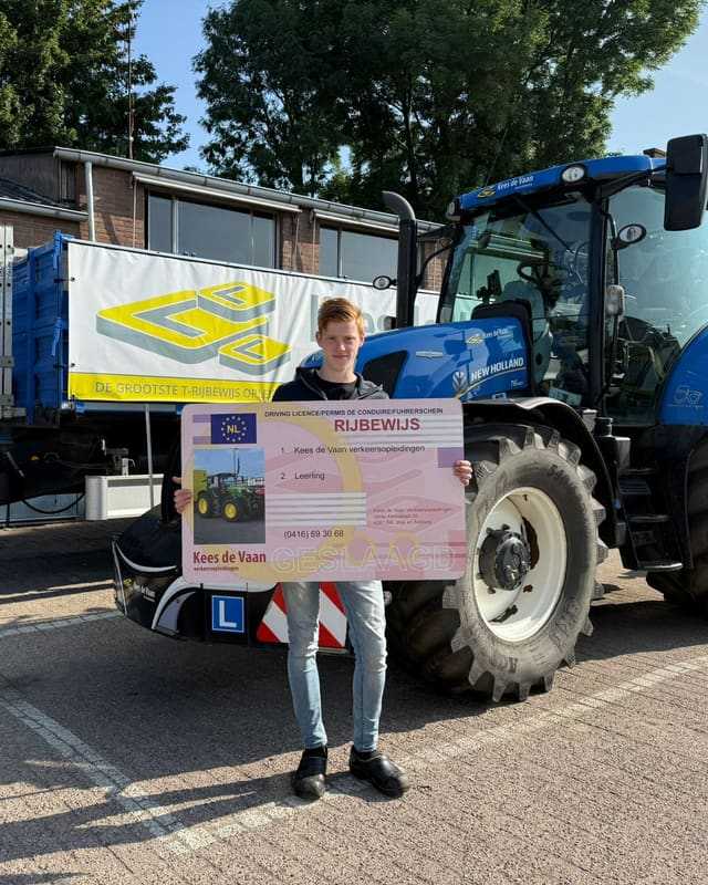 Geslaagd voor het T-rijbewijs: cursist met rijbewijsbord voor een blauwe lestrekker en de aanhangwagen van Kees de Vaan