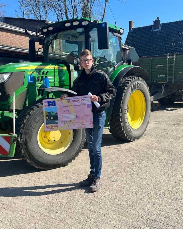 Geslaagd voor het trekkerrijbewijs: cursist met bril en rijbewijsbord naast een groene lestrekker
