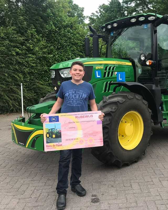 Geslaagde cursist in blauw T-shirt met rijbewijsbord voor een groene lestrekker