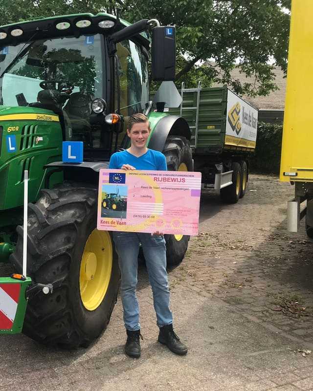 Geslaagd voor het T-rijbewijs: cursist met rijbewijsbord naast het voorwiel van een groene lestrekker